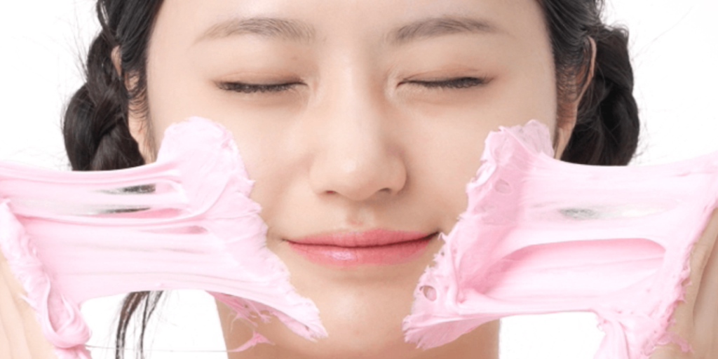 バズっている韓国コスメ:エイプリルスキン TXA ナイアシンアミド 99 ディープ クレンザーのテクスチャーを両手で伸ばして見せているイメージで、淡いピンク色のもっちりとした弾力のある質感が強調されている。モデルは目を閉じた穏やかな表情で、やさしい洗い心地を表現している。