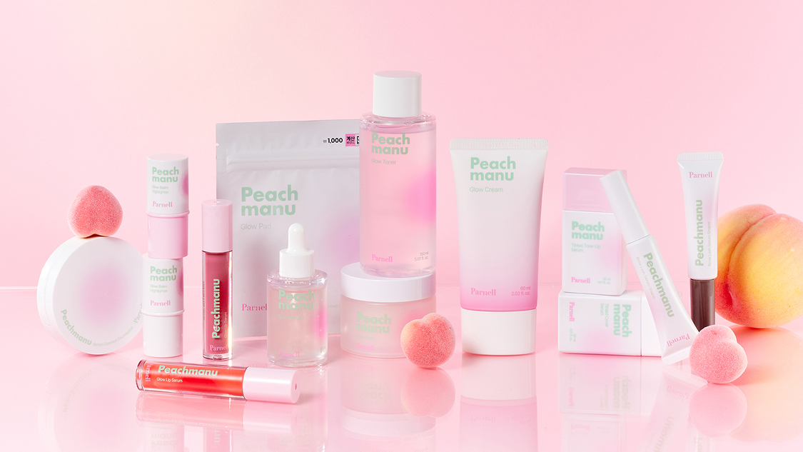 Peach manu skincare products arranged on a soft pink background, including toner, cream, serum, lip serum, and glow pads in pastel pink and white packaging, styled with small peach-shaped puffs and a real peach for a cohesive peach-themed aesthetic.