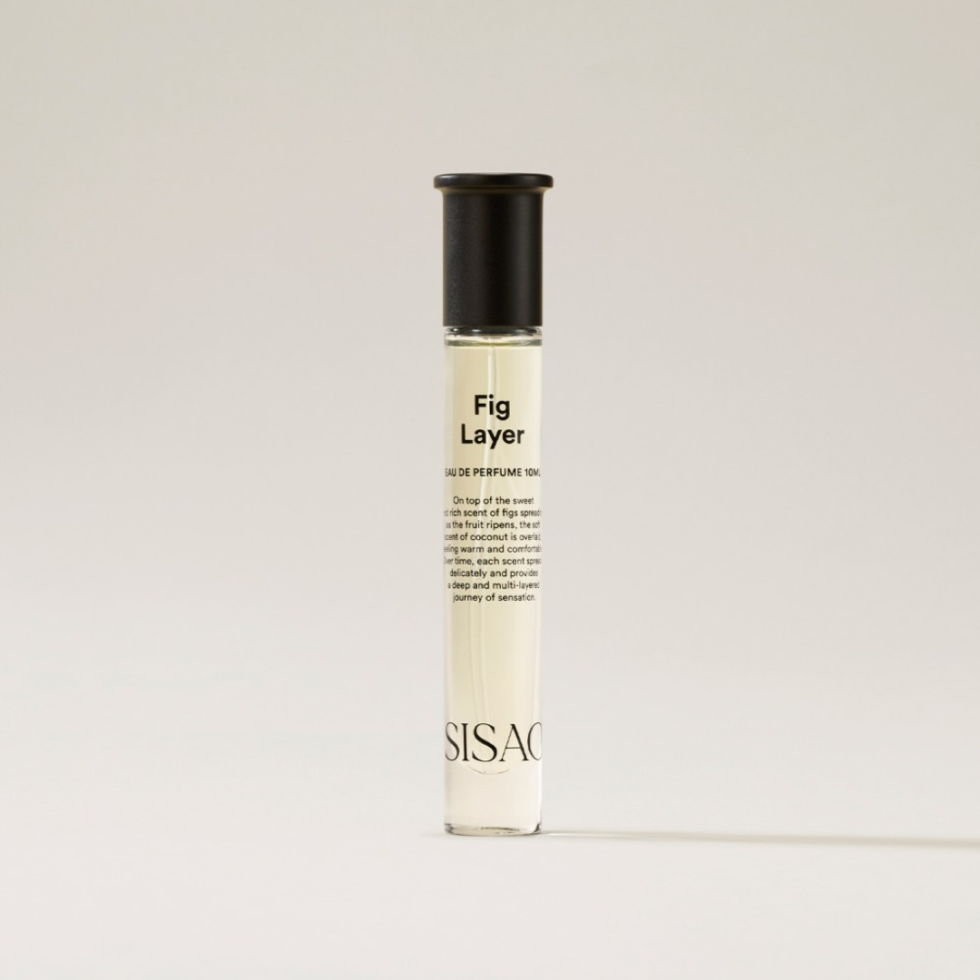 A minimal glass perfume bottle labeled “Fig Layer” from SISAO stands upright against a neutral beige background, showcasing its sleek and simple design.
