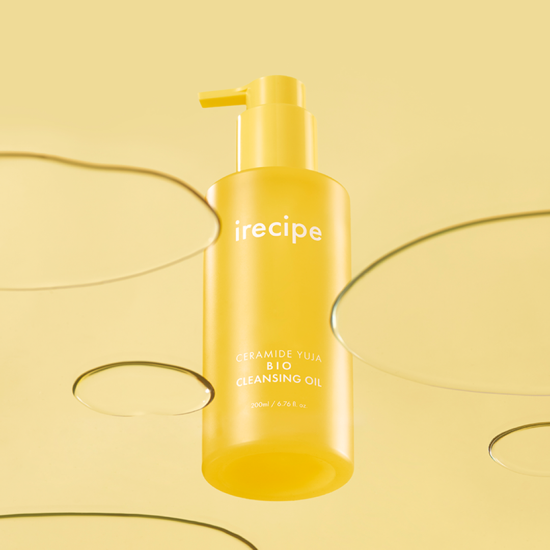 明るいイエロートーンの背景の中央に、鮮やかな黄色のポンプ容器に入った irecipe の Ceramide Yuja Bio Cleansing Oil が配置されている。周囲には透明なオイルのしずくが広がり、フレッシュでクリーンな雰囲気を演出している。