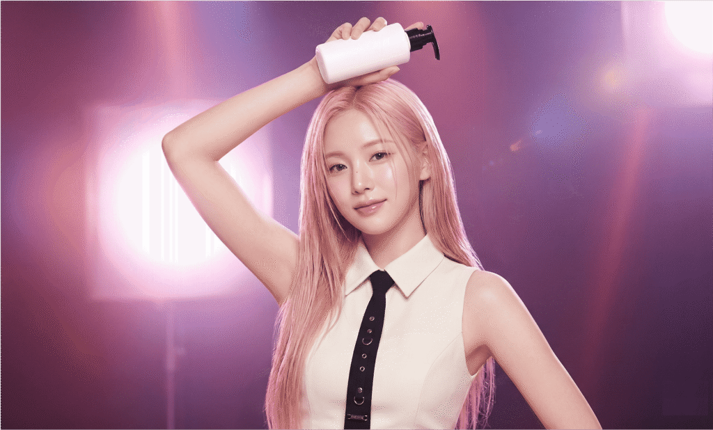 K-pop idol with pink hair applying hair care product on stage-style lighting background, illustrating a K-pop idol hair care routine.