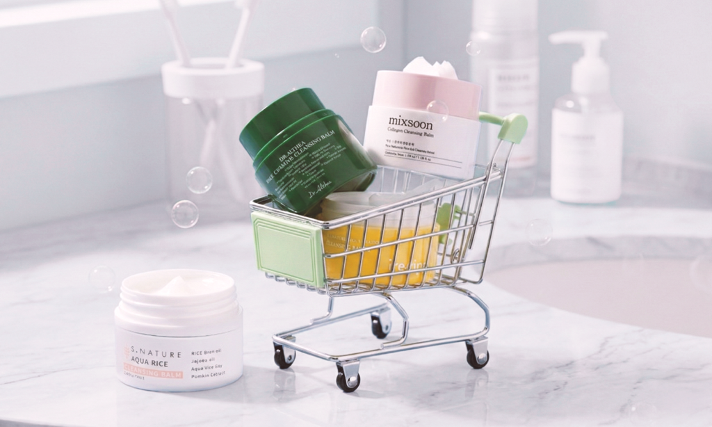 Assorted cleansing balm jars displayed in a mini shopping cart on a bathroom counter.
