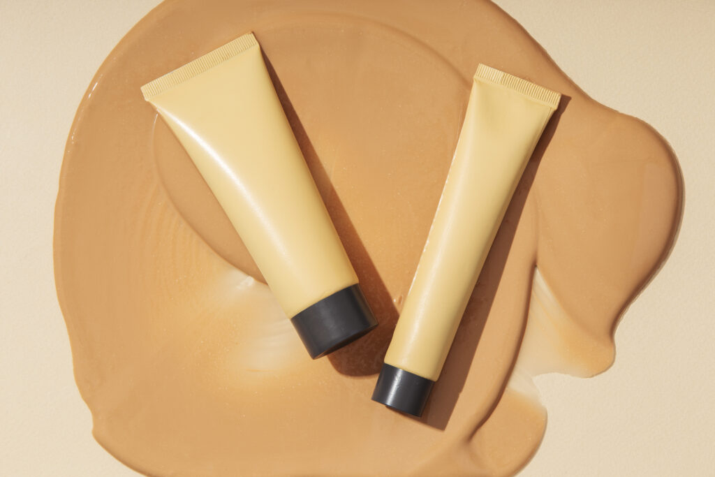 bb cream vs cc cream comparison showing two base makeup tubes placed on a beige foundation smear, highlighting differences in texture and coverage finish