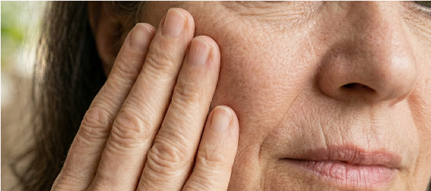 A woman gently touching her cheek, showing visible fine lines and loss of skin firmness
