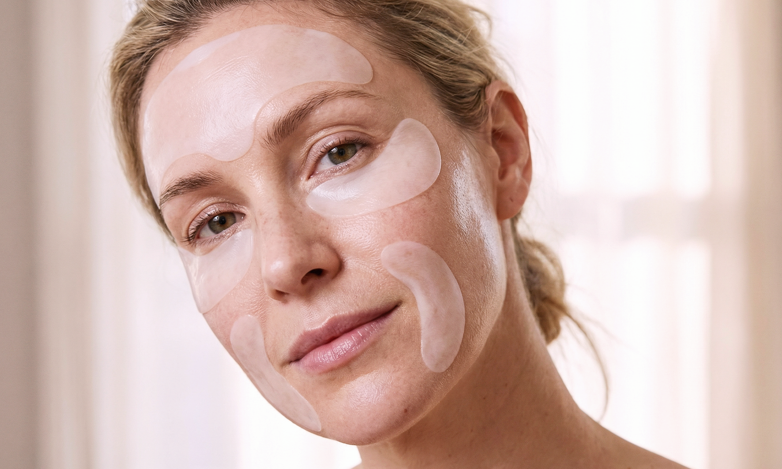 Mujer usando parches antiarrugas en la frente, el contorno de ojos y las mejillas como parte de una rutina de cuidado antiedad para hidratación localizada y alisado visual de la piel.